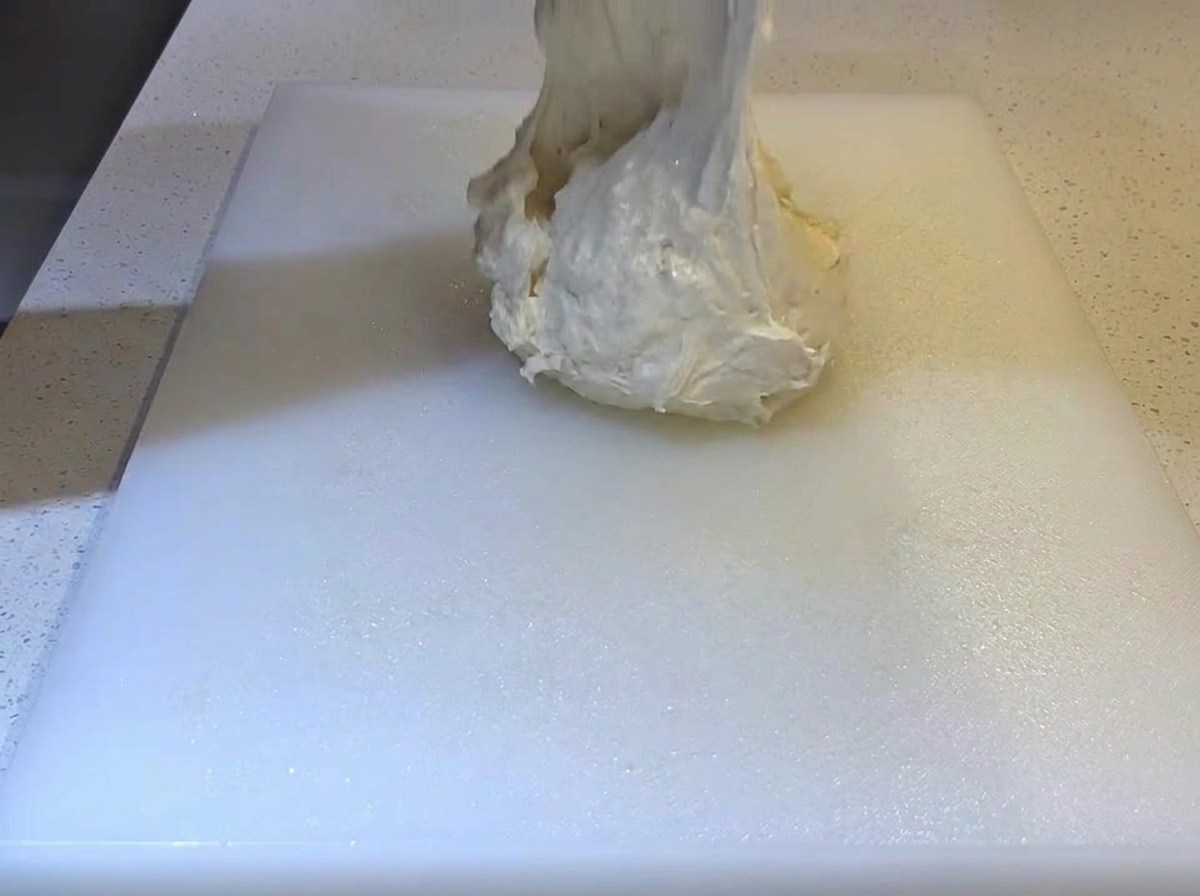 Masa suave y pegajosa cayendo sobre una tabla de cortar blanca engrasada.