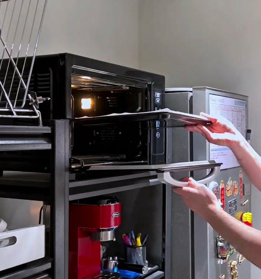Una persona introduciendo una bandeja con masa de pizza cruda y pinchada en un horno doméstico caliente.
