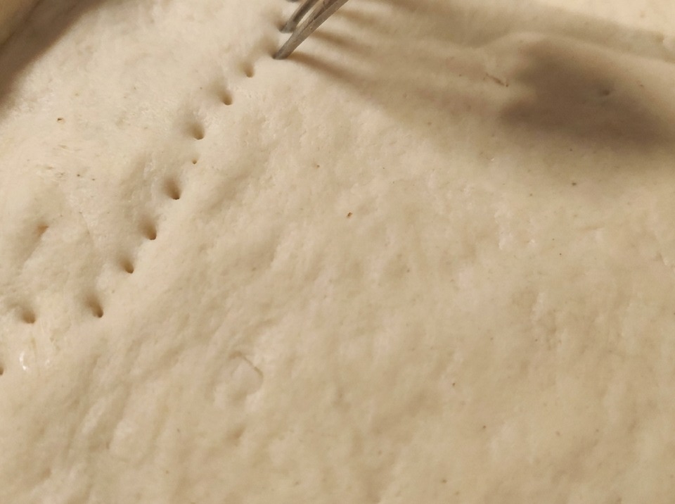 Un tenedor presionando sobre la masa cruda para crear filas de agujeros en la corteza.