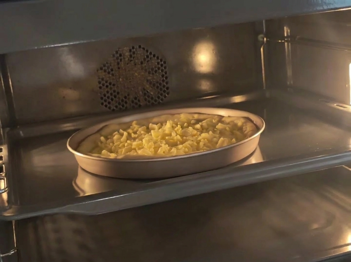 Un molde con masa de pizza preparada y queso dentro de un horno precalentado.