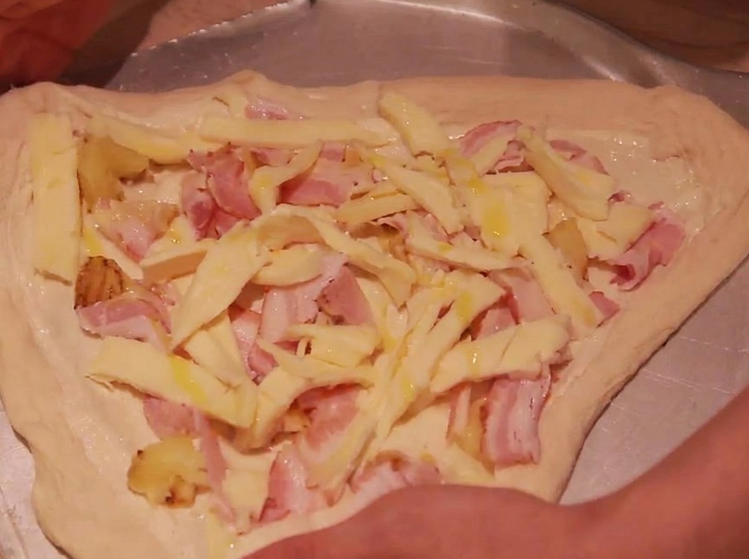 Los bordes de la masa de pizza doblándose hacia adentro para encerrar los ingredientes.