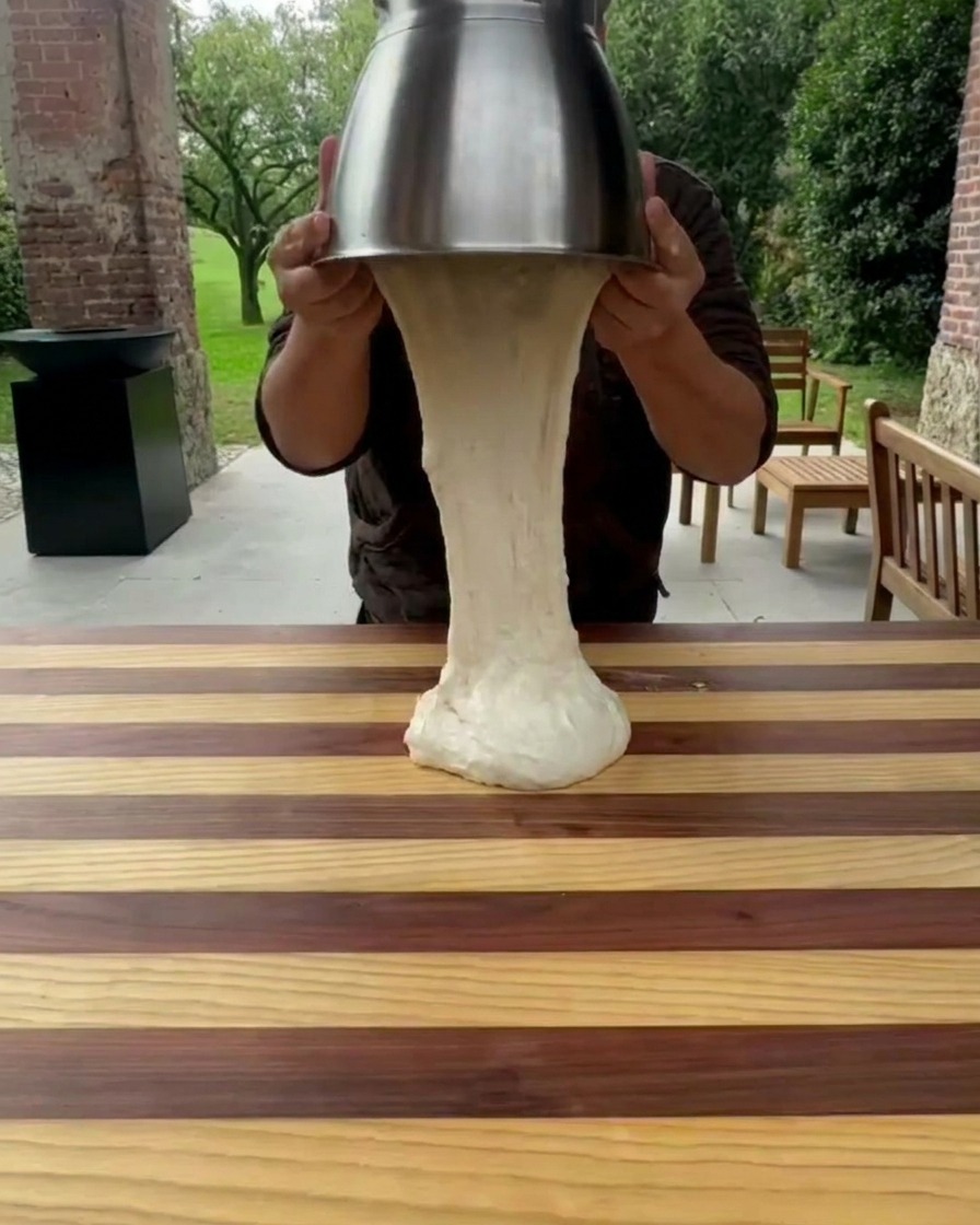 Masa siendo levantada de un tazón de acero inoxidable hacia una encimera de madera.