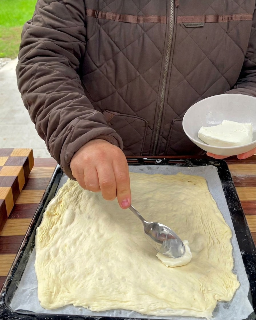 Base de queso cremoso siendo extendida sobre la masa con una cuchara.