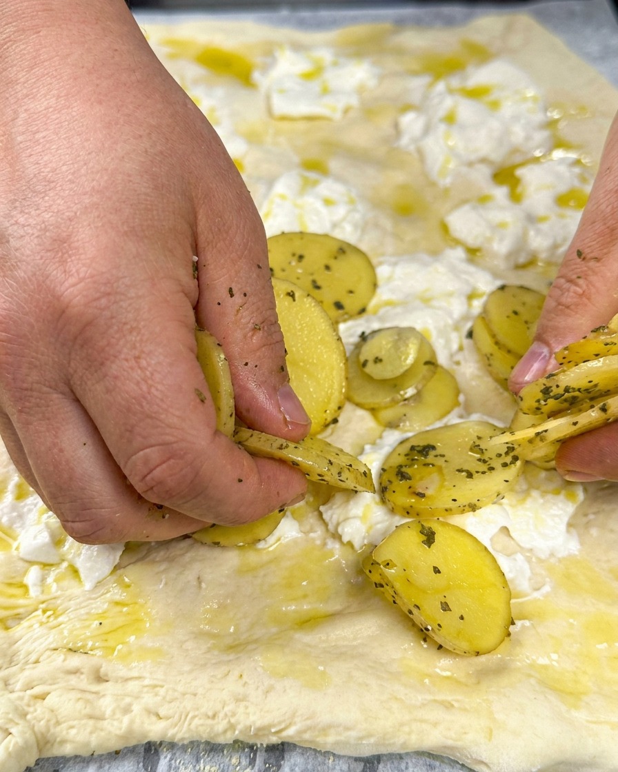 Rodajas de patata dispuestas sobre la base de queso y cubiertas con hierbas frescas.