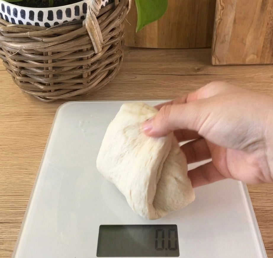 Una porción de masa de pan blanca y suave sobre una báscula de cocina digital que muestra el peso.