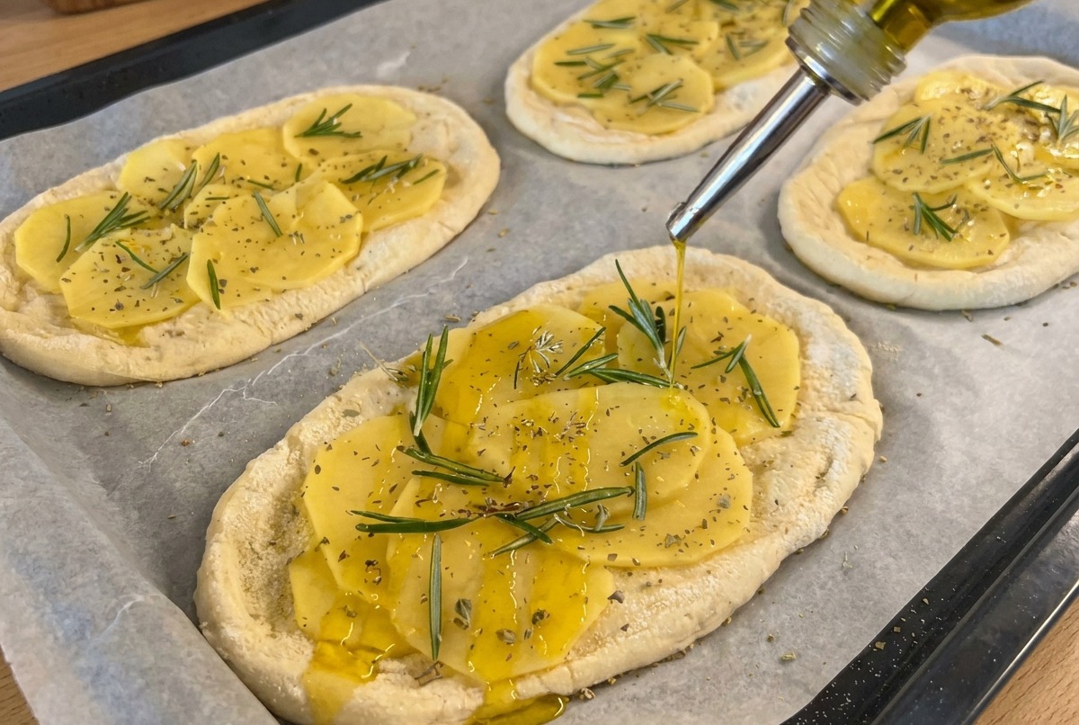 Aceite de oliva siendo rociado desde una botella sobre la masa cubierta de patatas, con sal añadida desde un molinillo.