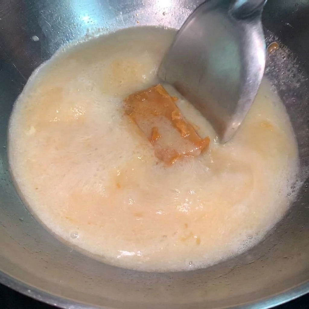 Una cucharada de salsa de miso concentrada siendo mezclada en una olla con caldo de ramen a fuego lento.