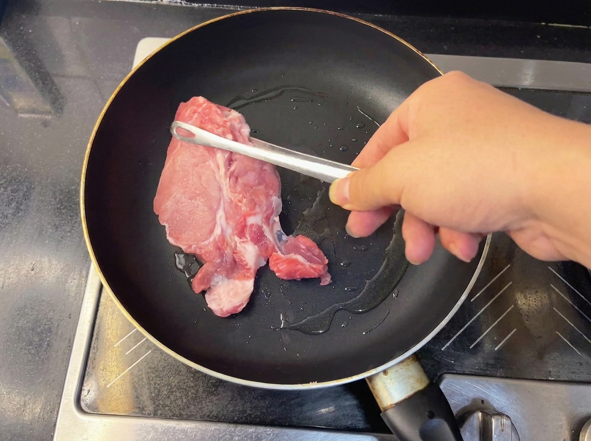 Dos piezas de carne de cerdo cruda sellándose en una sartén caliente.