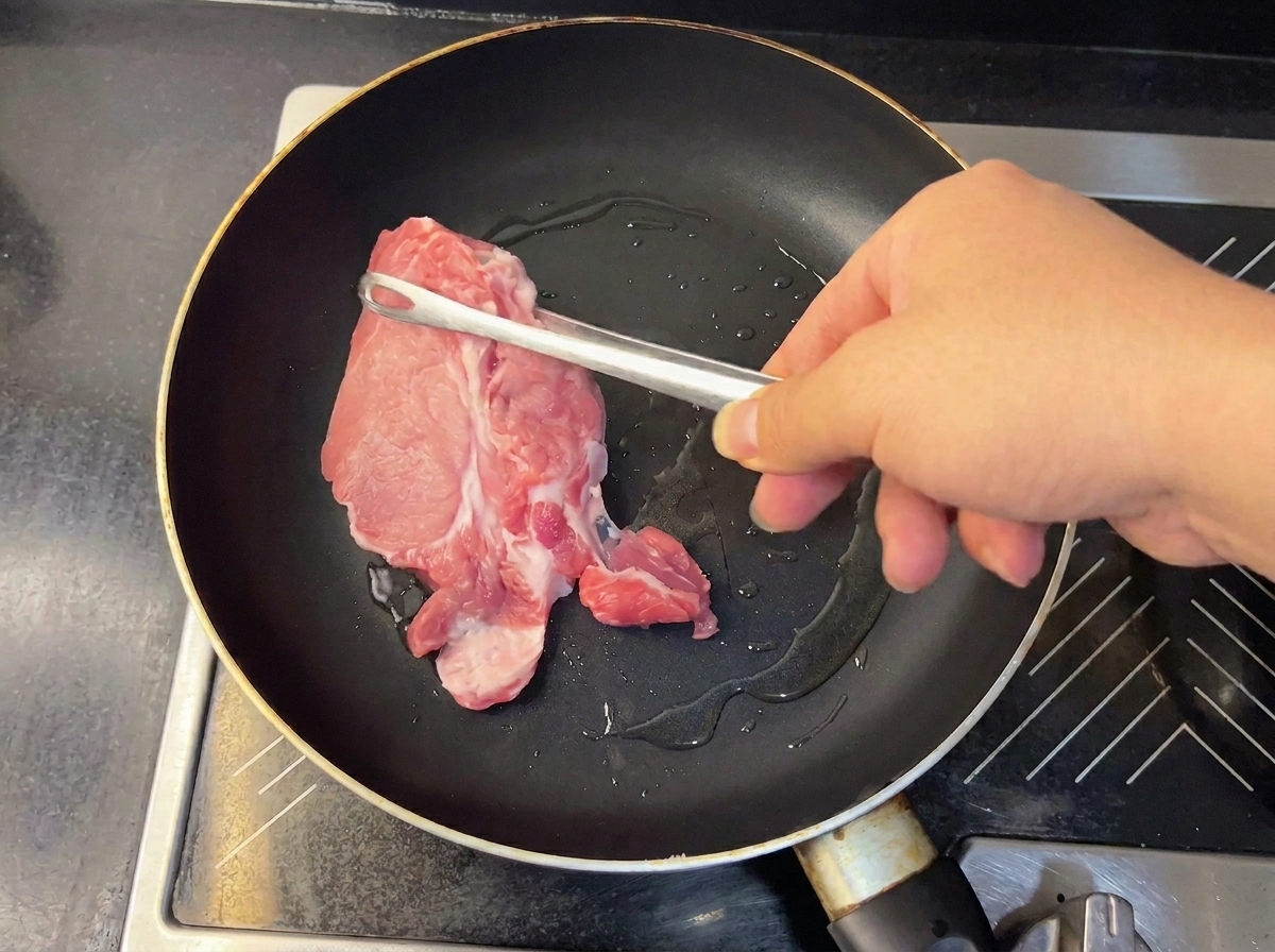 Piezas de cerdo tierno y dorado retirándose de la sartén con pinzas.