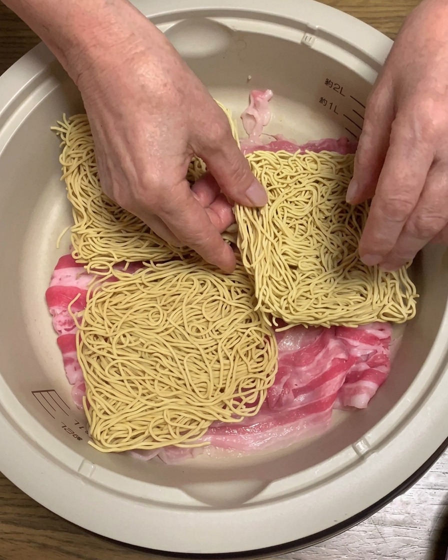 Bloques de fideos de ramen secos colocados sobre la panceta dentro de la olla.