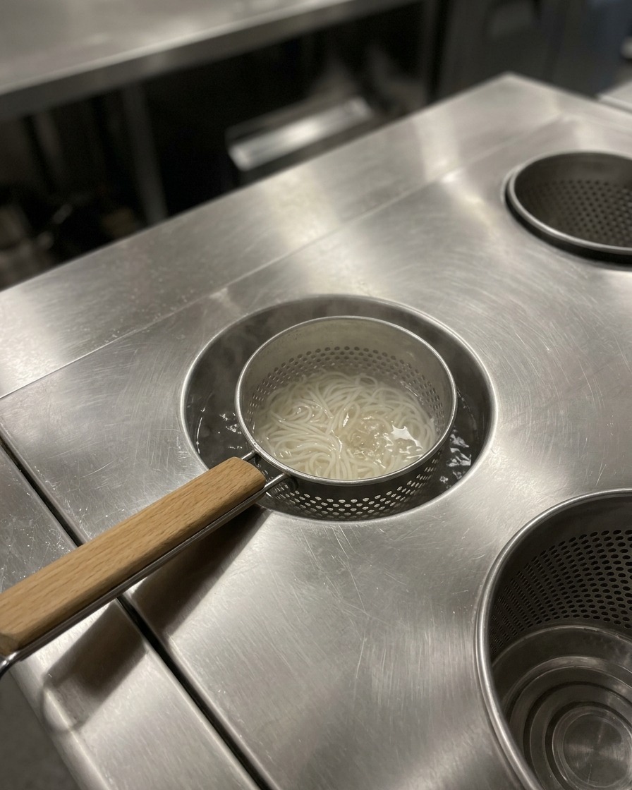 Fideos ramen cocidos dentro de un tazón de servir, siendo preparados para la adición del caldo caliente.