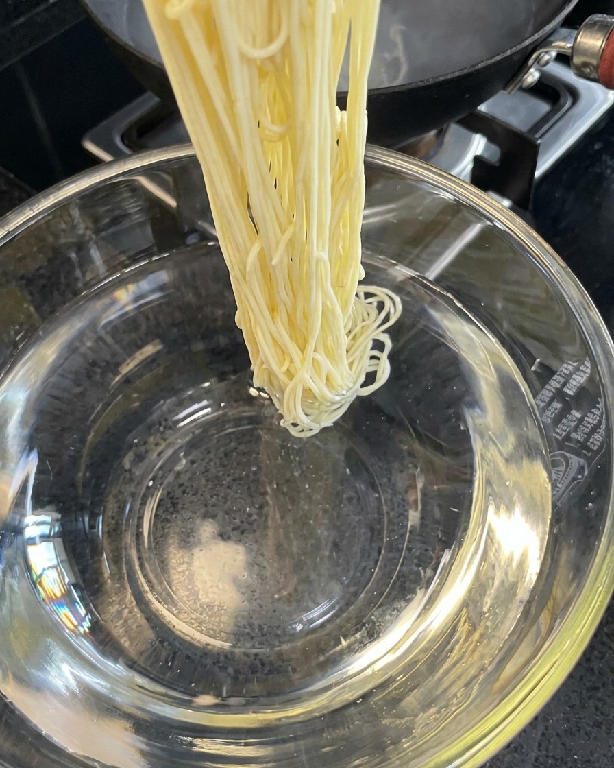 Fideos cocidos siendo enjuagados en un bol con agua fría.