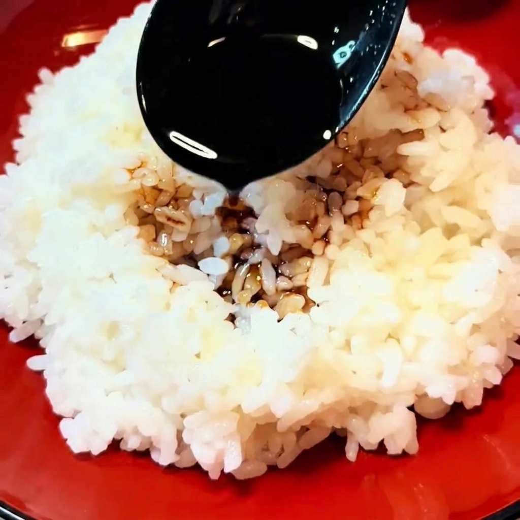 Una cuchara negra rociando salsa marrón sobre un tazón de arroz blanco humeante.