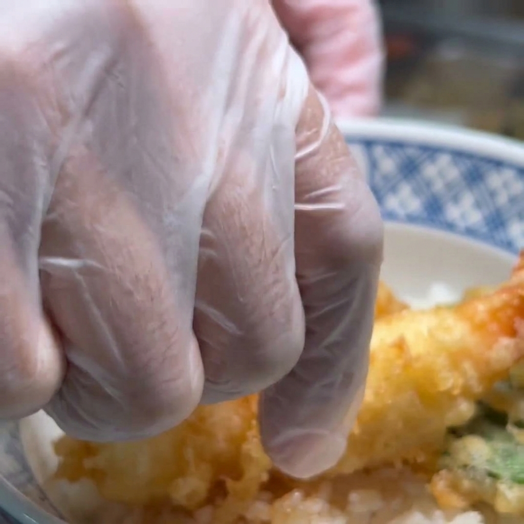 Camarones fritos siendo colocados sobre una cama de arroz blanco en un tazón, listos para decorar.