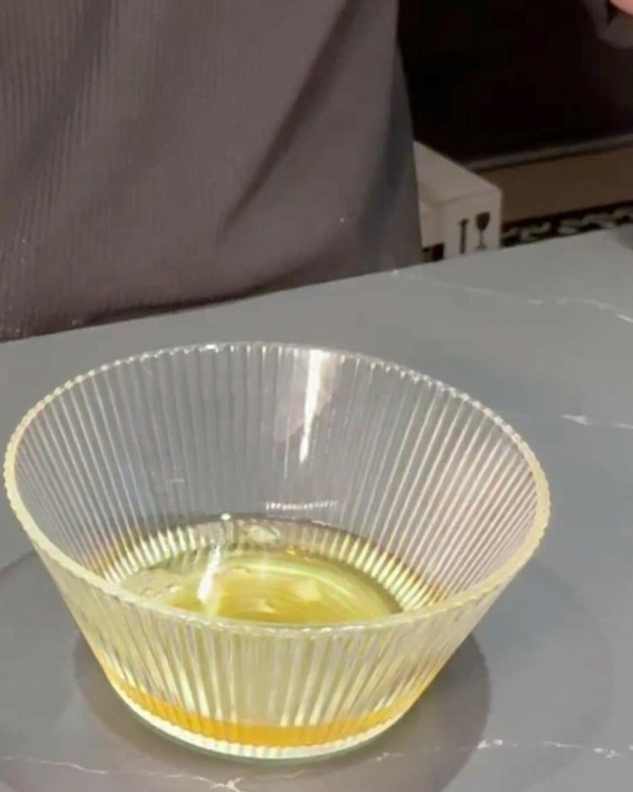 Mirin y salsa de soja siendo vertidos en un tazón de vidrio transparente que contiene caldo dashi.
