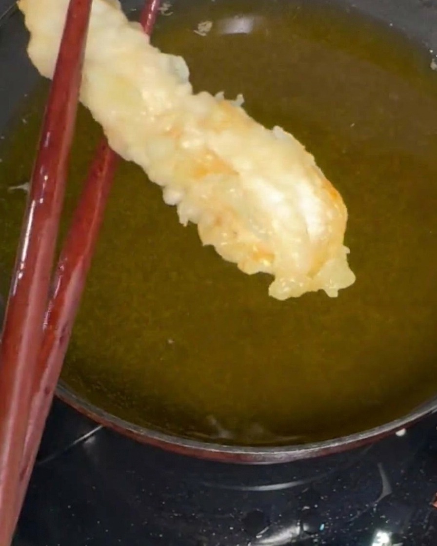 Camarones siendo rebozados en la masa después de un ligero espolvoreado de harina seca.