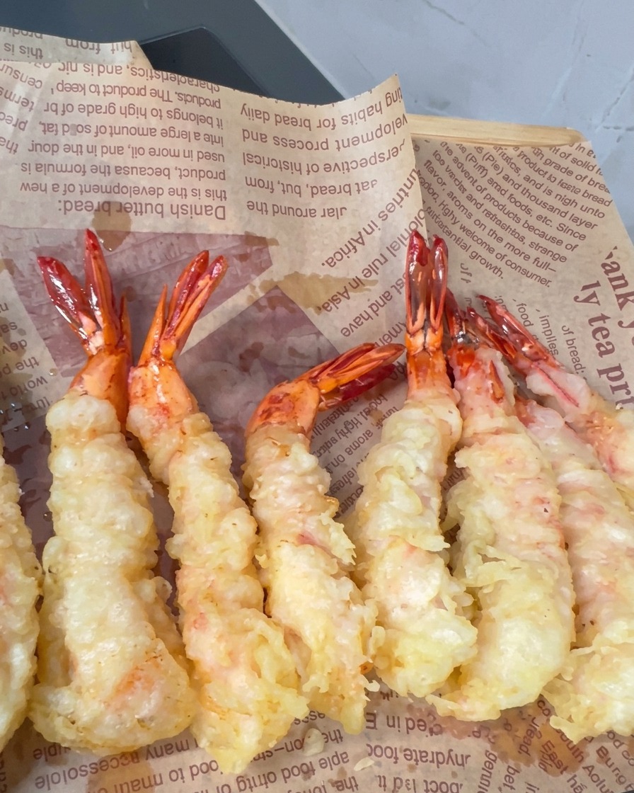 Camarones rebozados friéndose en aceite caliente con picos crujientes formándose en la superficie.