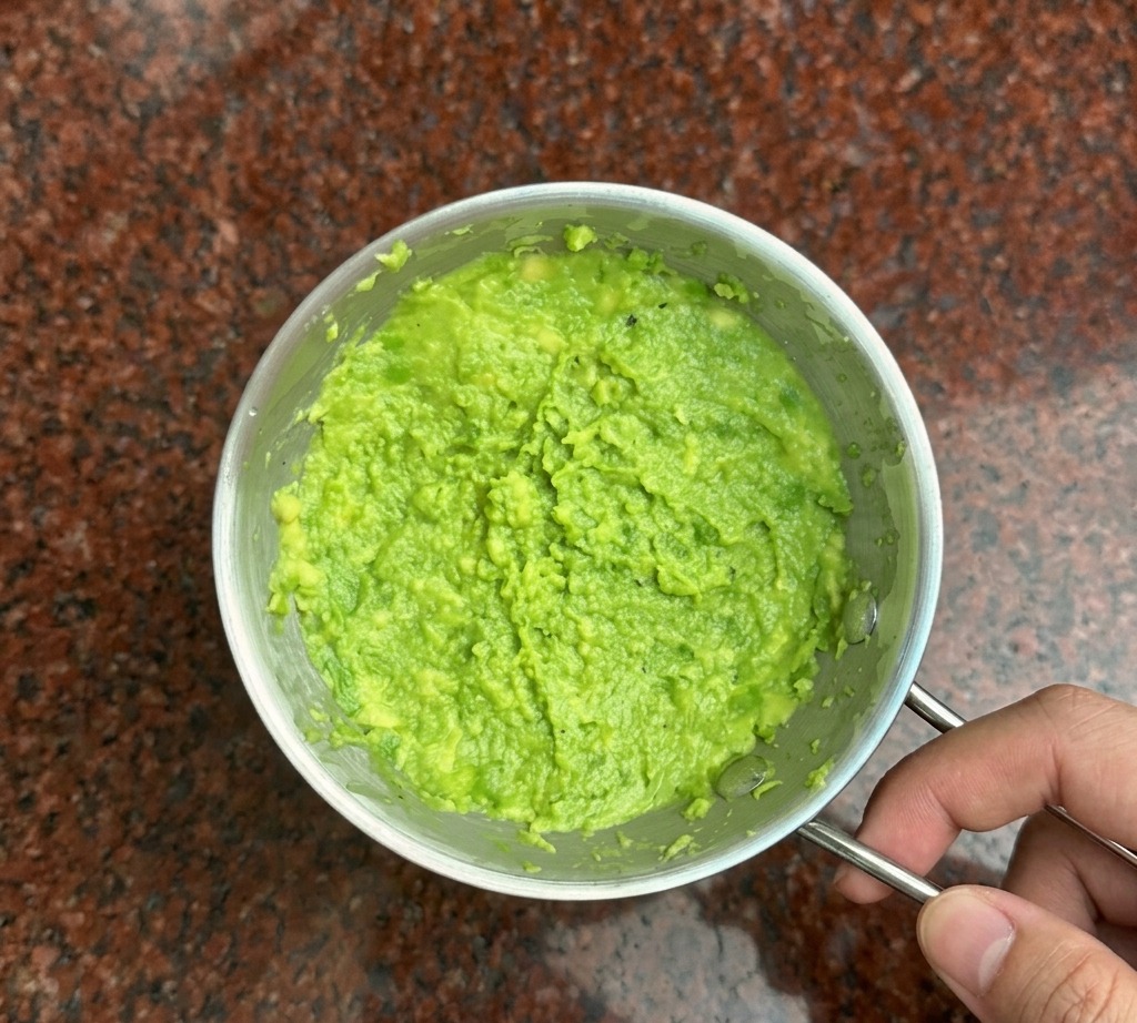 Un tenedor de metal machacando aguacate de color verde brillante hasta formar una pasta espesa en un bol pequeño.