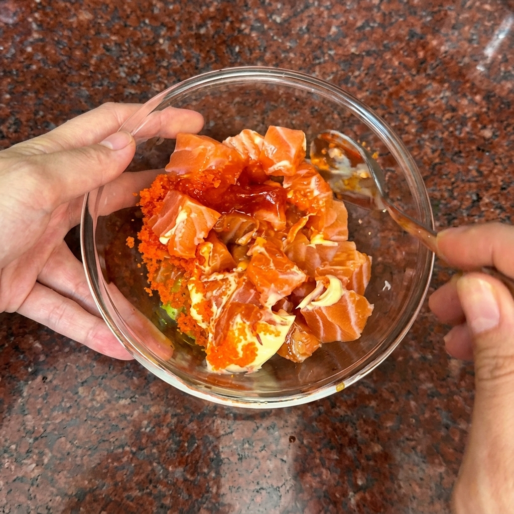 Una mano removiendo los cubos de salmón junto con una salsa cremosa de color naranja usando una cuchara.