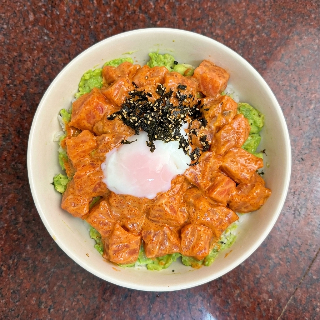 Una vista zenital de un poke bowl de salmón coronado con un huevo poché y aderezo de alga oscura.