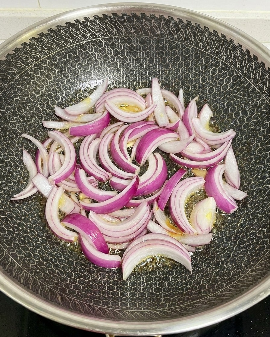 Tiras de cebolla morada salteándose en un wok caliente con aceite brillante.