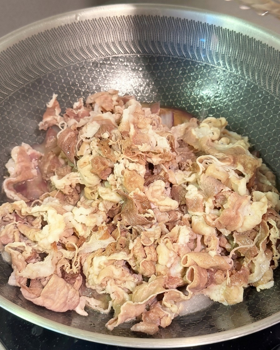 Tiras de ternera blanqueada mezclándose con cebolla morada y salsa oscura en un wok de acero inoxidable.