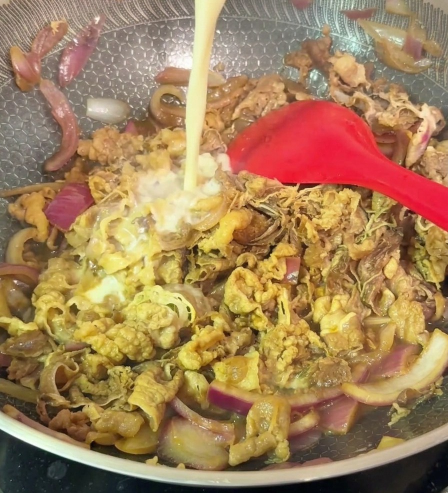 Un hilo de mezcla líquida de almidón vertiéndose en un wok con ternera salteada y cebolla morada.