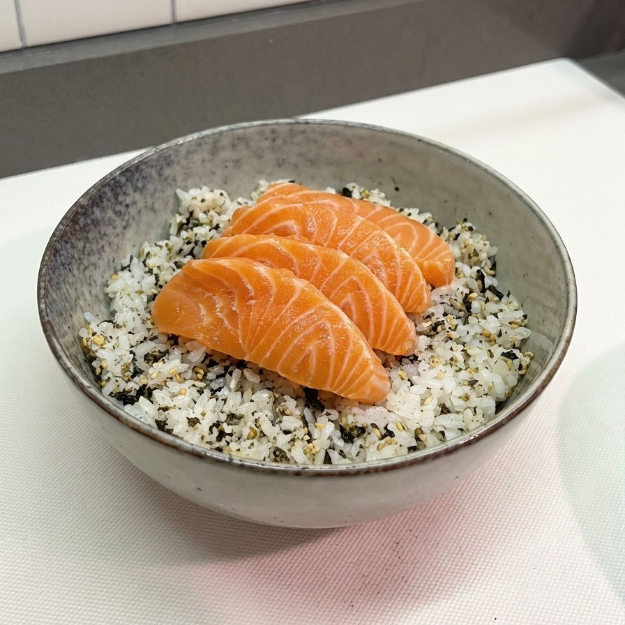 Cuatro láminas gruesas de salmón de color naranja brillante dispuestas sobre una cama de arroz blanco con copos de alga nori en un cuenco cerámico gris.