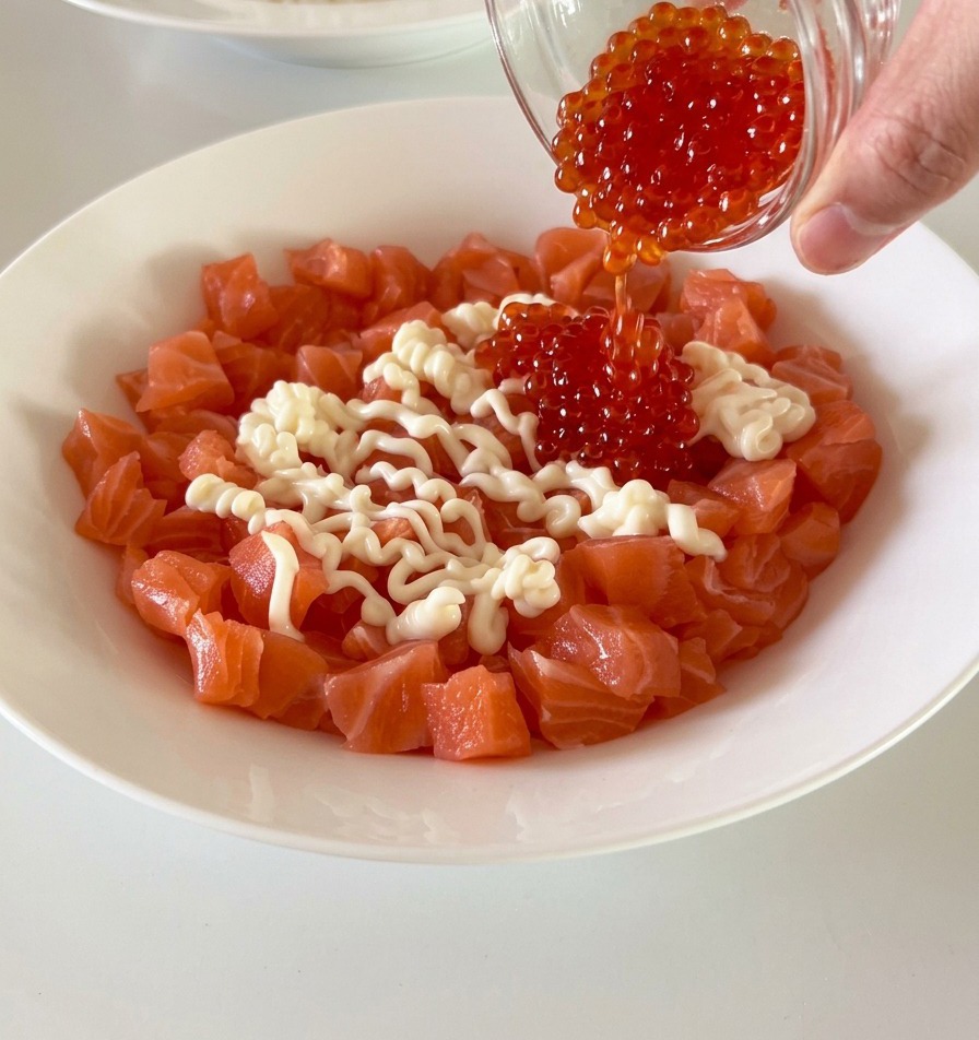 Dados de salmón fresco en un tazón blanco coronados con huevas de pescado de color rojo brillante y mayonesa.