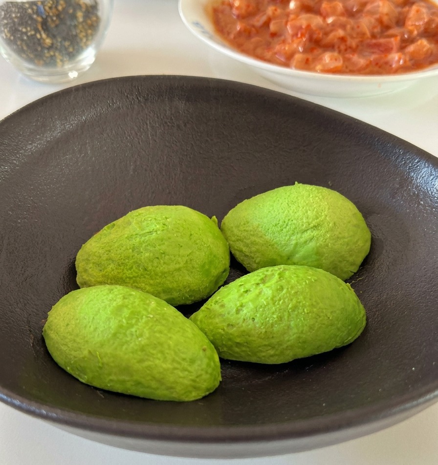 Una mano exprimiendo un gajo de limón fresco sobre mitades de aguacate en un cuenco de cerámica.