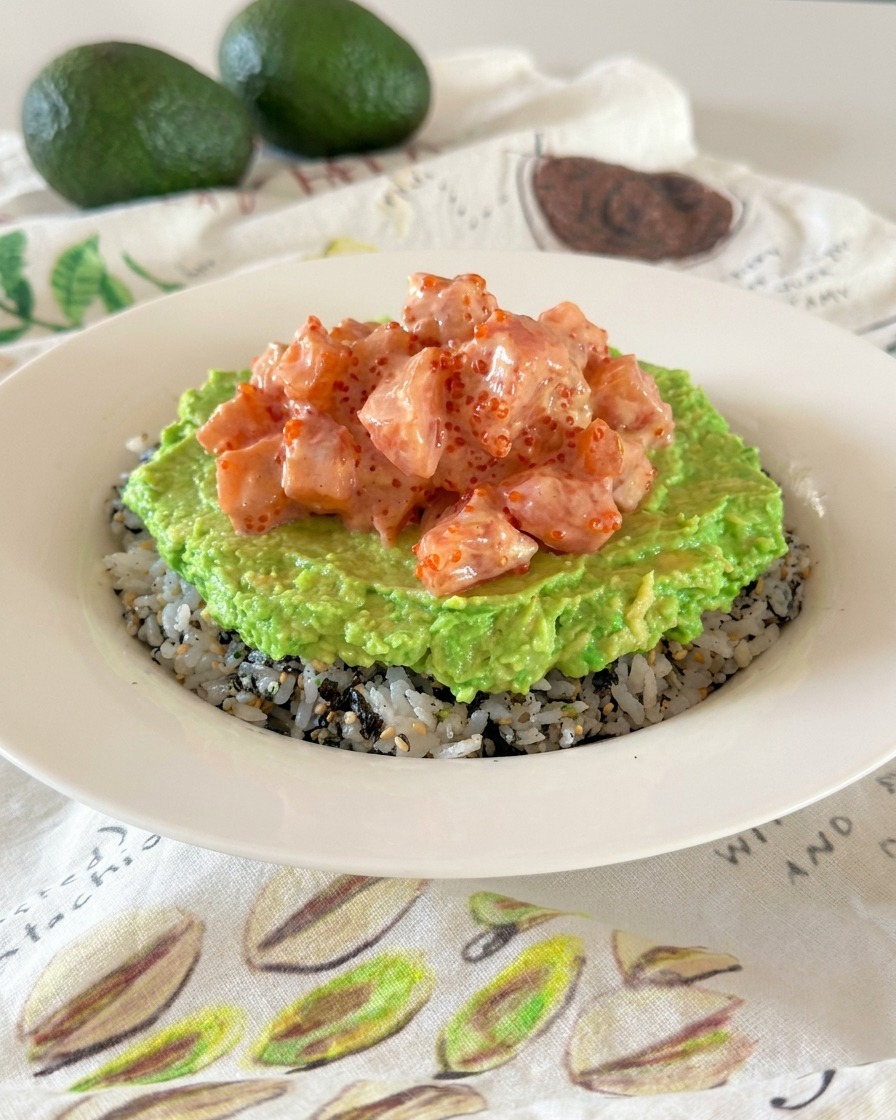 Un tazón de poke que muestra capas diferenciadas de arroz sazonado, aguacate triturado y dados de salmón cremoso.