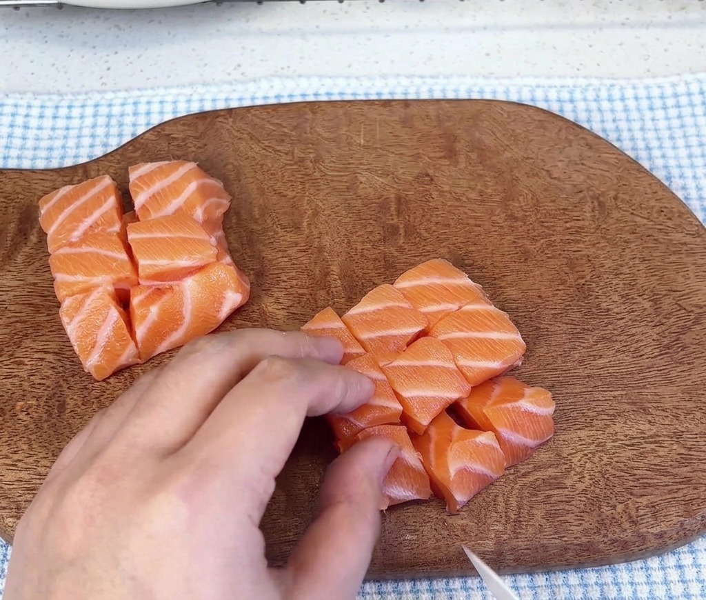 Varios montones de cubos de salmón crudo sobre una tabla de cortar de madera después de haber sido fileteados.
