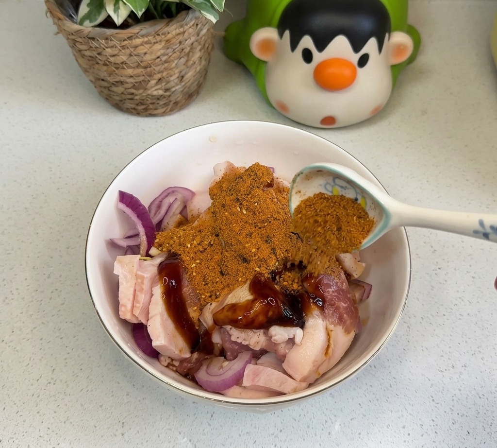 Una cucharada de sazonador de barbacoa de color naranja y chile en polvo espolvoreándose sobre la panceta de cerdo marinada.