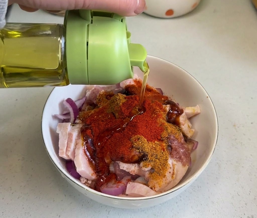 Aceite de cocina transparente cayendo desde una botella verde sobre la mezcla de panceta de cerdo con especias.