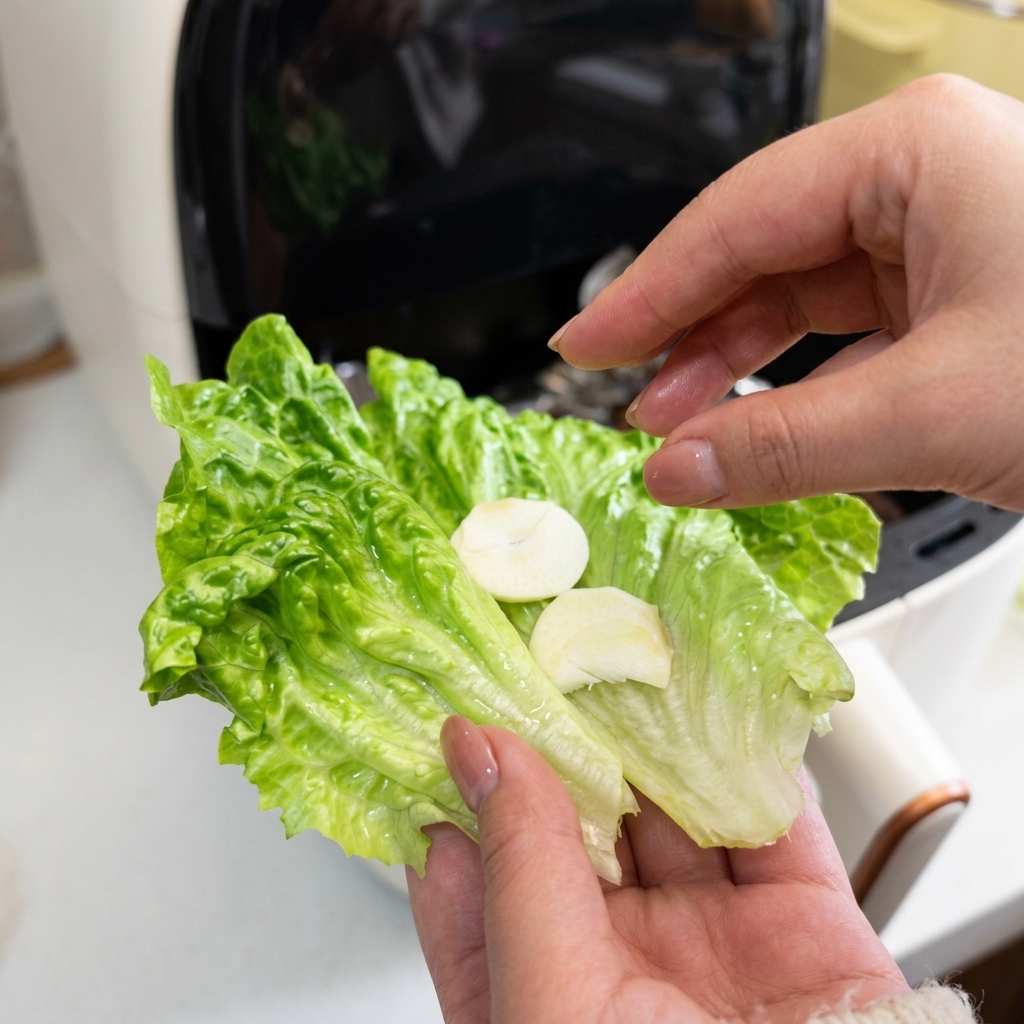 Primer plano de una mano sosteniendo una hoja verde de lechuga con dos láminas de ajo blanco fresco encima.