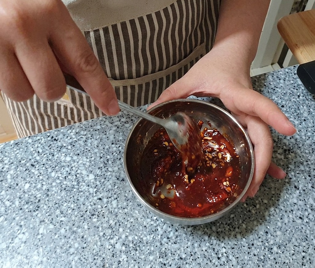 Removiendo un marinado espeso de color rojo intenso en un bol de metal con una cuchara de acero inoxidable hasta que esté bien integrado.