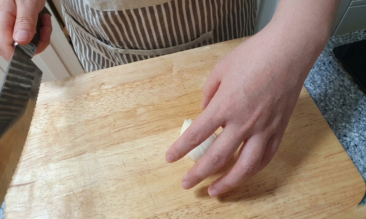Uso de un cuchillo para hacer cortes finos y verticales en una cebolla blanca sobre una superficie de madera.