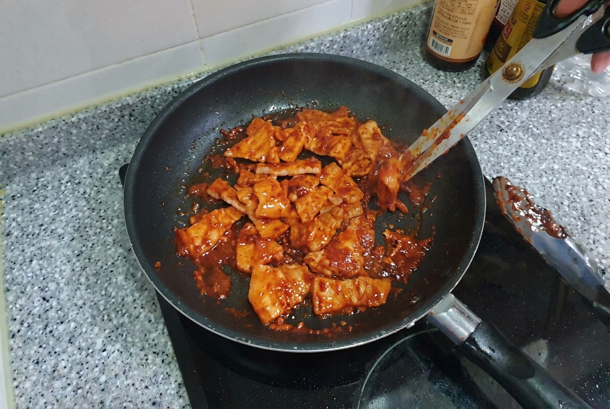 Trozos pequeños de panceta de cerdo picante salteándose en una sartén, con un aspecto brillante y caramelizado.
