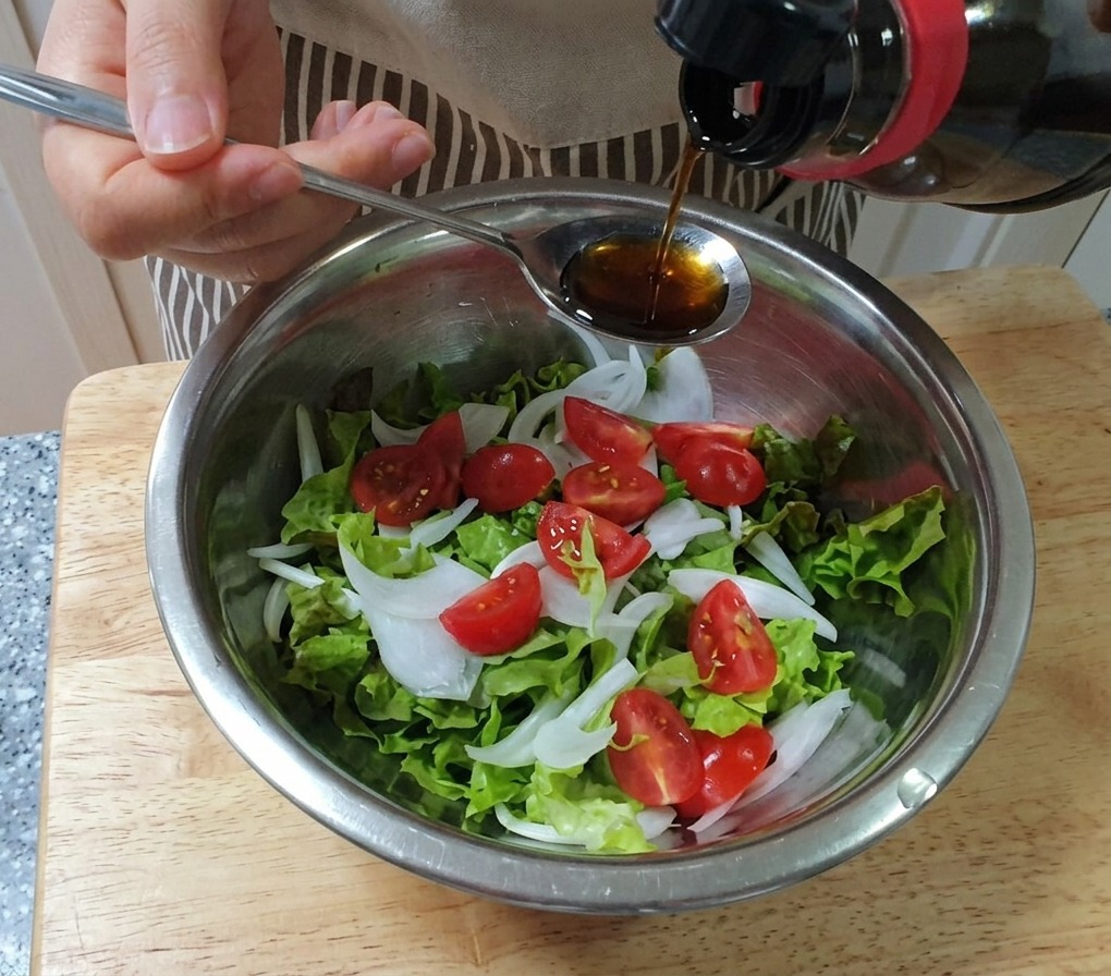 Aderezo vertiéndose desde una cuchara sobre un bol con lechuga, cebolla y tomates cherry.