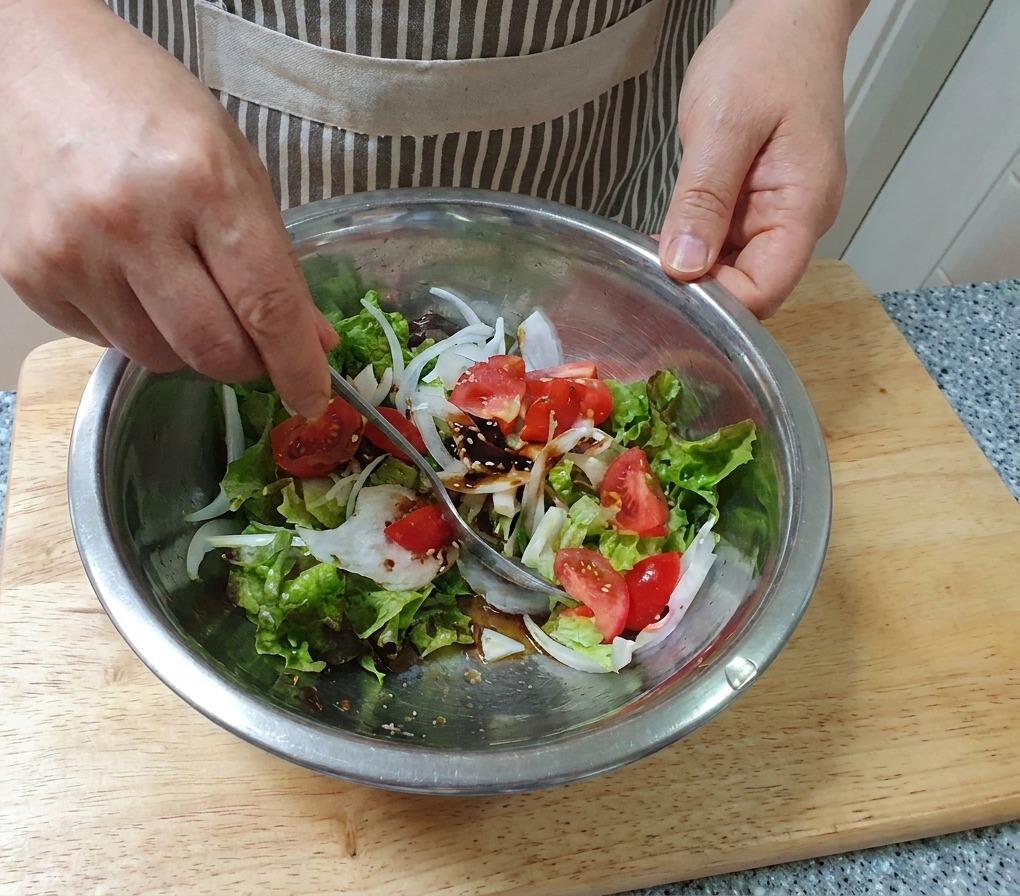 Una mano mezclando una ensalada de verduras frescas con una cuchara en un bol grande de acero inoxidable.