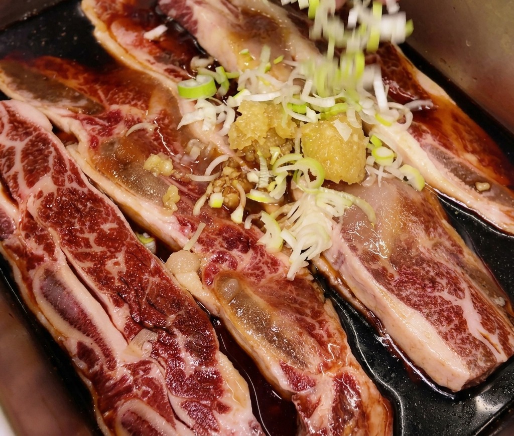 Cebollines picados siendo esparcidos a mano sobre una bandeja de costillas de res crudas ya sazonadas con ajo y jengibre.