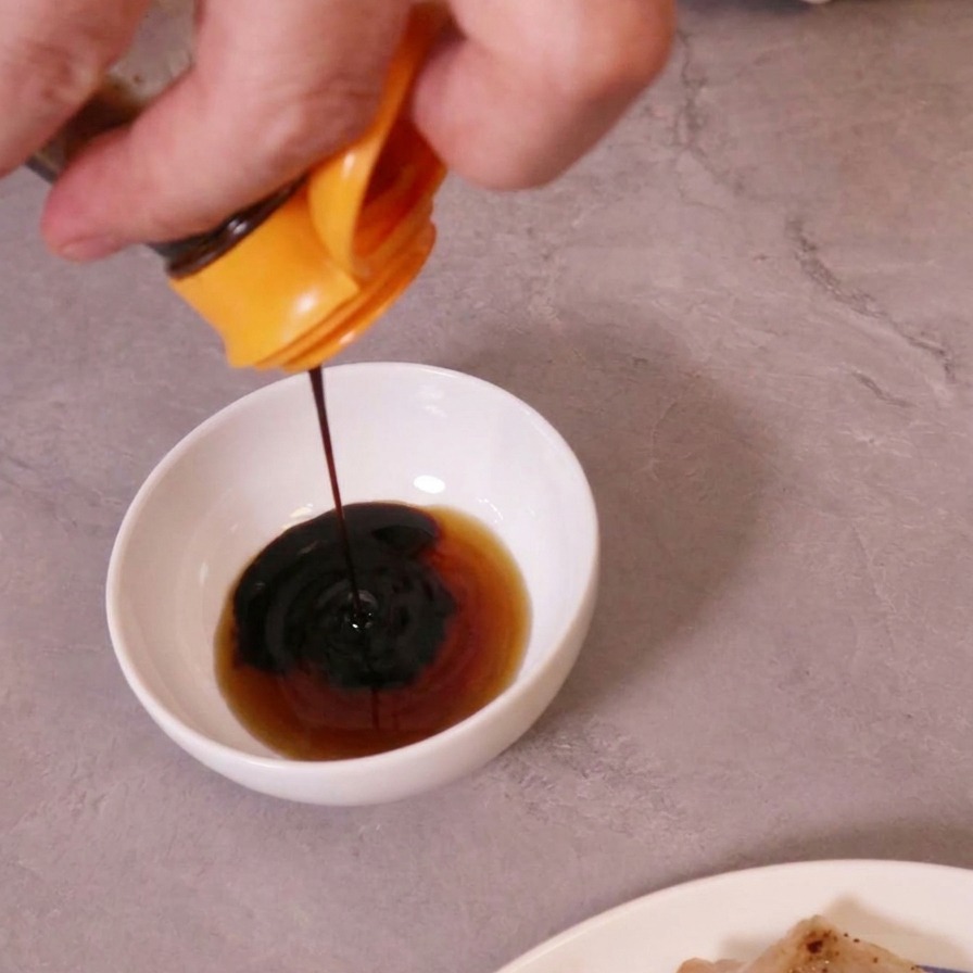 Salsa de soja vertiéndose en un cuenco blanco que contiene un líquido más claro para preparar una salsa para mojar.