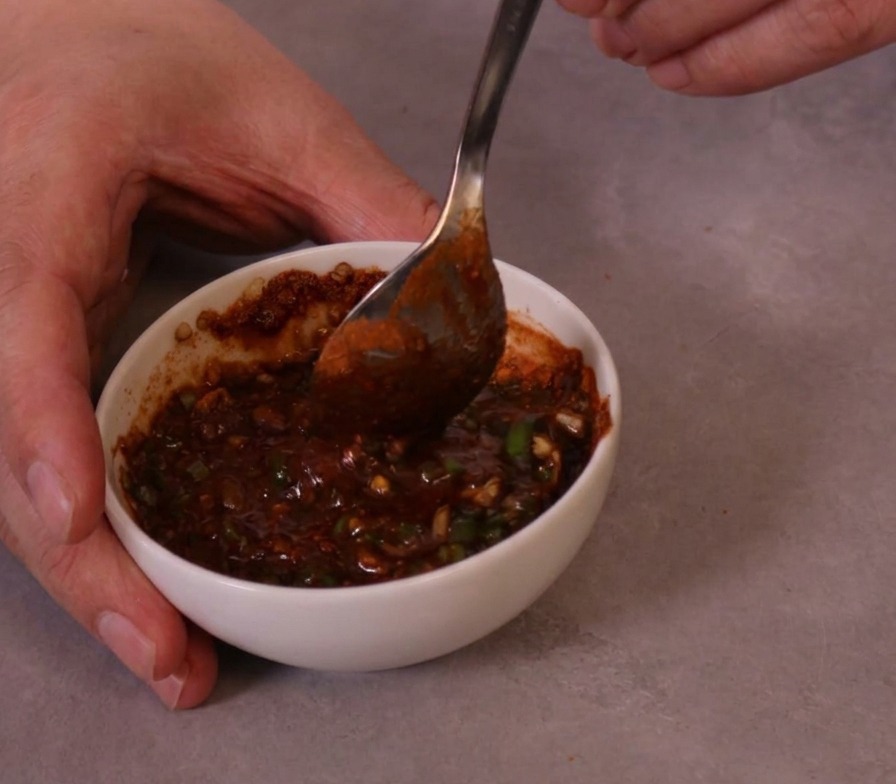 Una salsa espesa y de color rojo vibrante mezclándose con una cuchara de metal en un pequeño cuenco de cerámica.