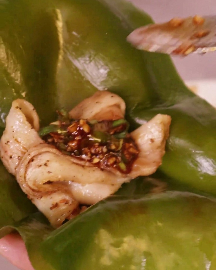 Salsa picante de chile rojo colocándose sobre un trozo de panceta a la parrilla que descansa en una hoja de alga kelp verde.
