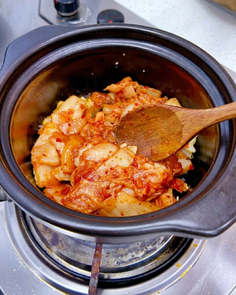 Una porción de kimchi de col picado agregándose a una olla con ajo salteado.