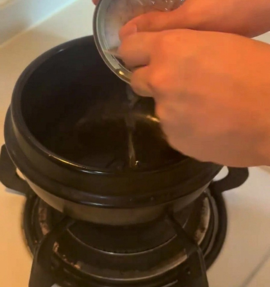 Aceite sabroso vertiéndose directamente desde una lata metálica de atún en una olla de cerámica oscura sobre la estufa.