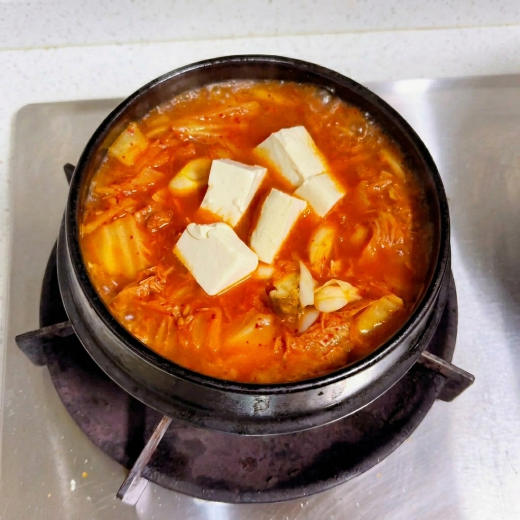 Cubos de tofu blanco fresco reposando sobre un caldo rojo de kimchi que hierve en una olla negra.