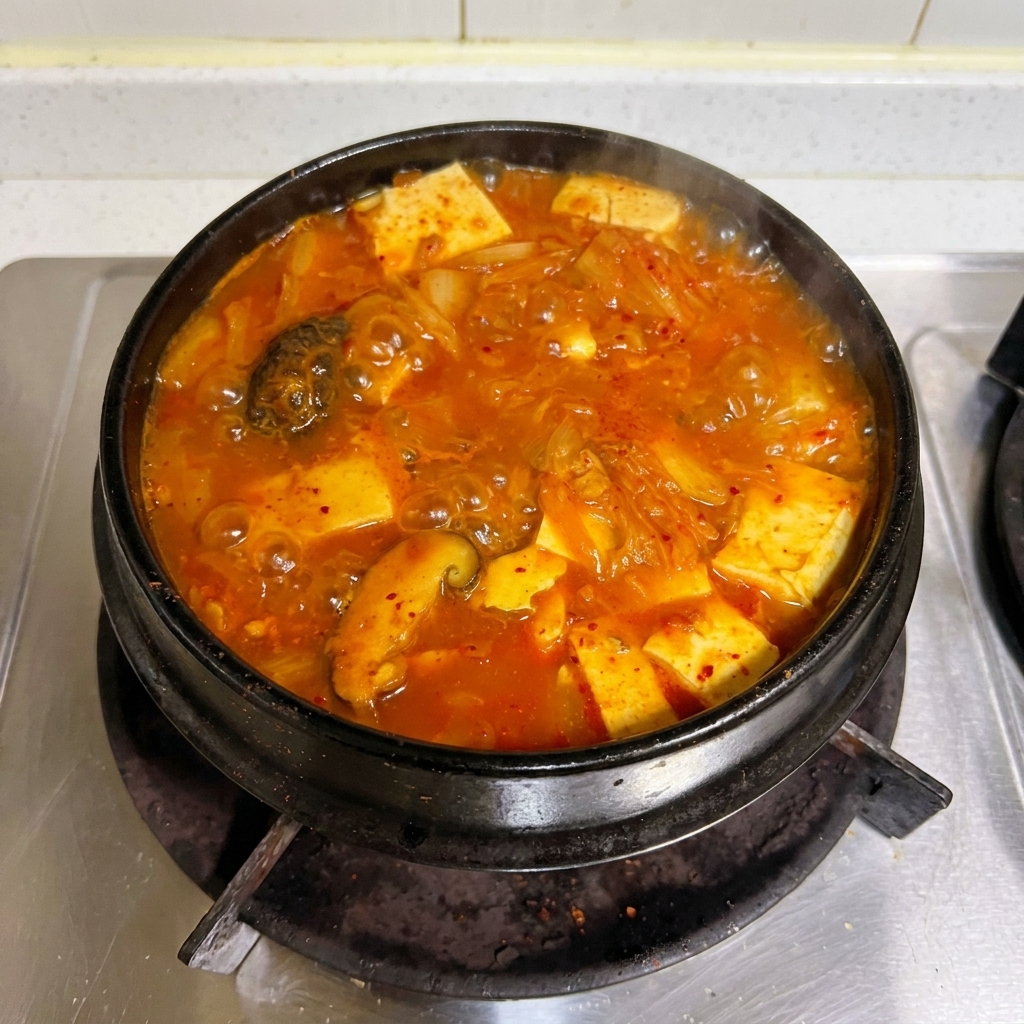 Un vistoso estofado rojo de kimchi y atún burbujeando con fuerza en una cazuela de piedra tradicional sobre la estufa.