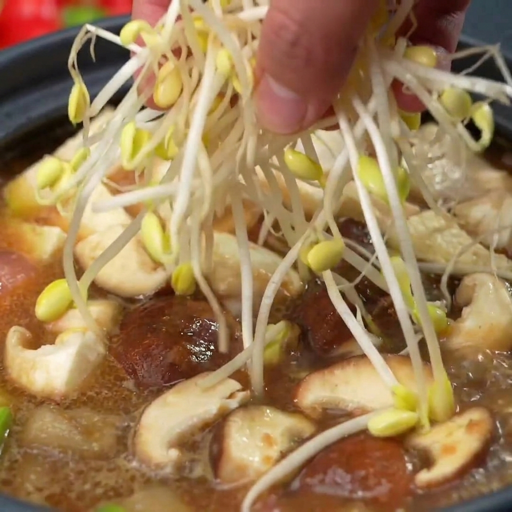 Una mano colocando un puñado de brotes de soja frescos y pálidos en la olla sobre los hongos y otros ingredientes de la sopa.