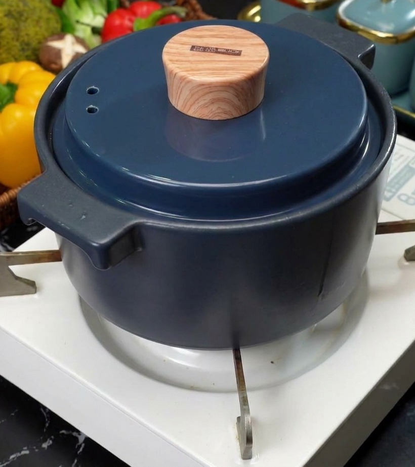 Una olla de cerámica azul con una tapa elegante con aspecto de madera colocada sobre el quemador de una estufa portátil blanca.